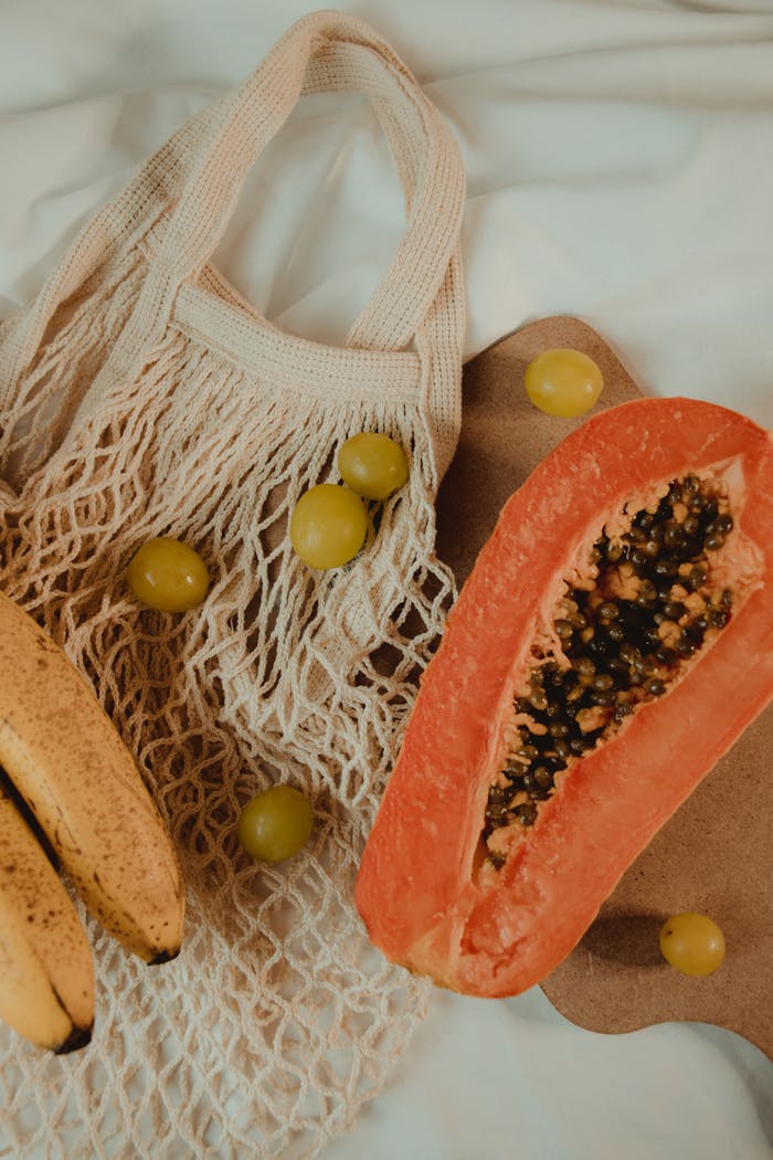Top view of a reusable bag with fresh papaya, bananas, and grapes.
